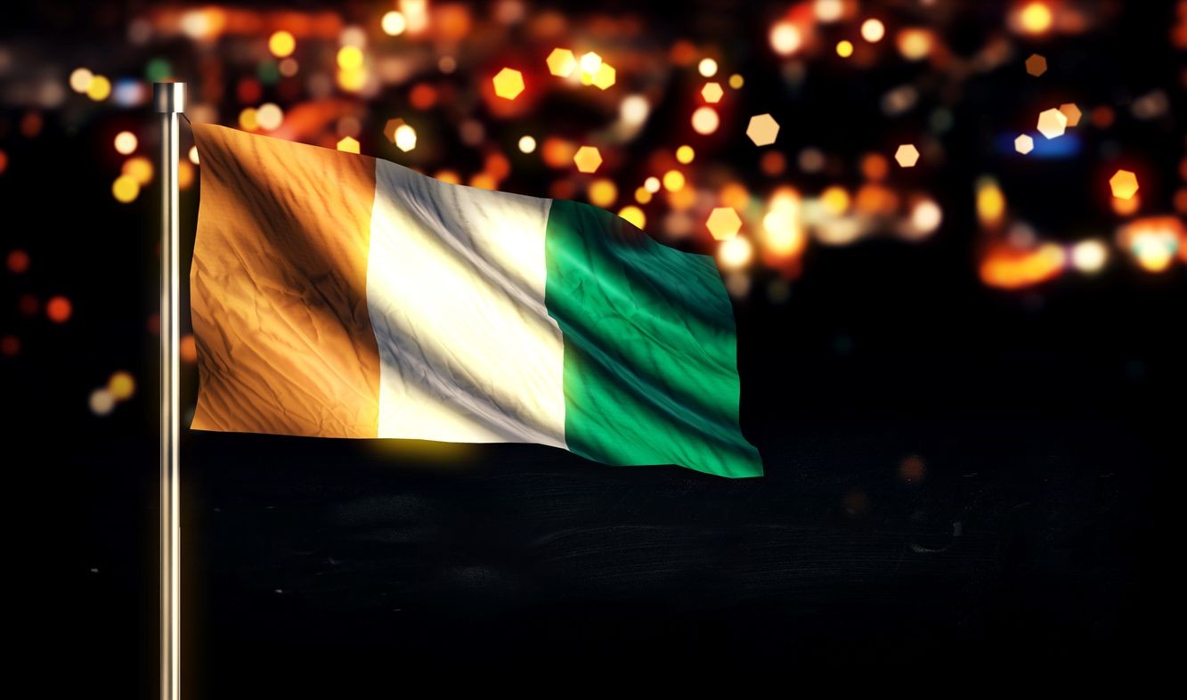 Flag of Ivory Coast waving on a flagpole with a blurred background of colorful lights at night.