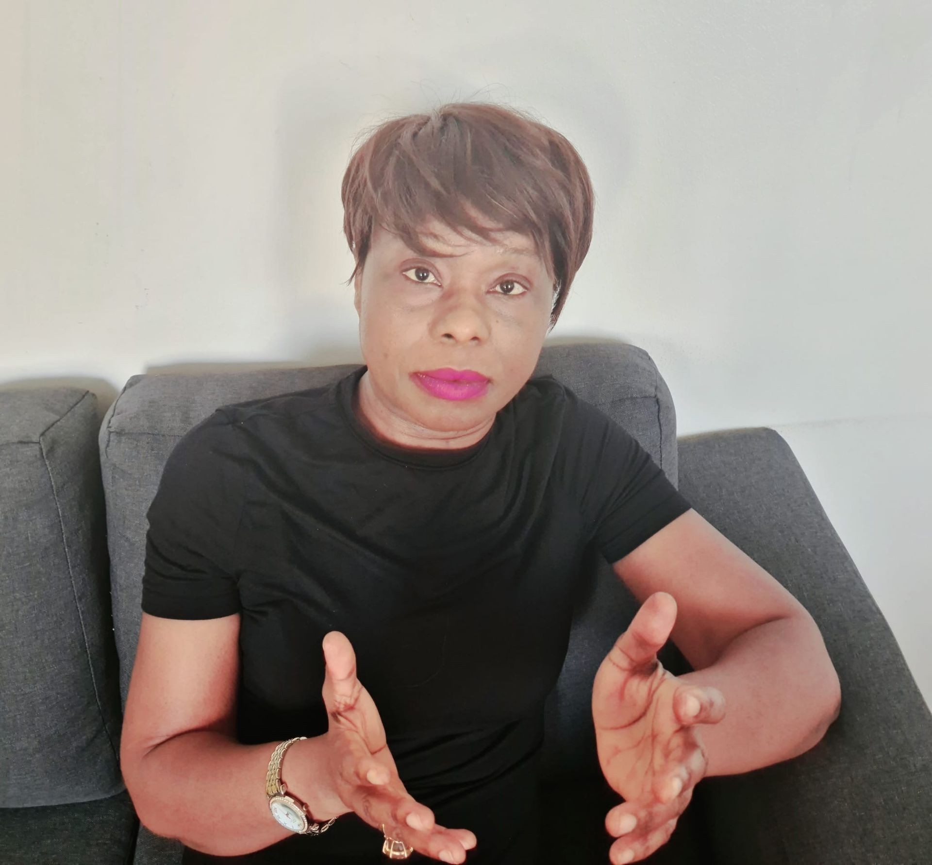 Person wearing a black shirt, sitting on a gray sofa, gesturing with their hands.