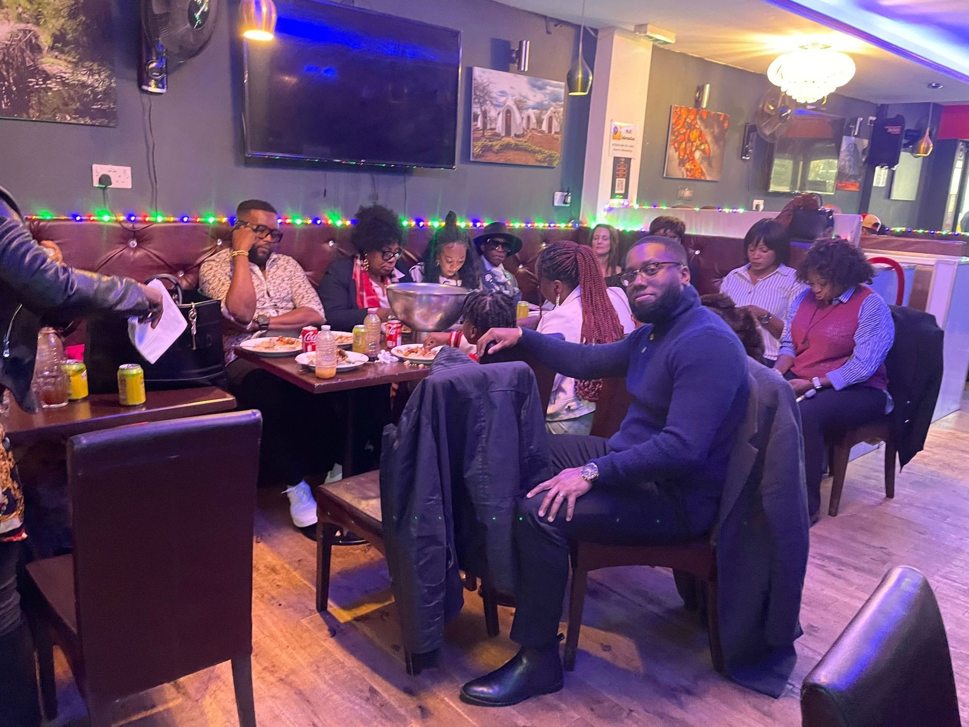 Group of people sitting and enjoying a meal in a cozy restaurant with ambient lighting and colorful decorations.